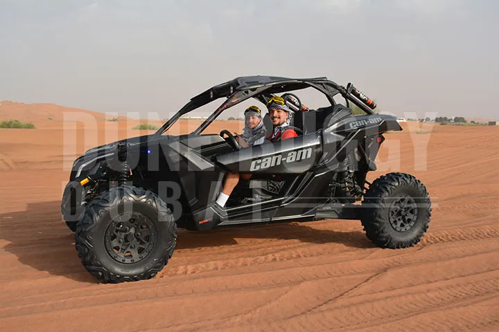 A black Can-Am Buggy Speeding Through A Desert along with 2 people inside.